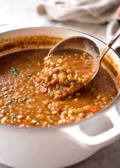 a ladle full of beans being spooned into a white pot filled with soup