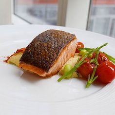 a white plate topped with fish and vegetables on top of a table next to a window