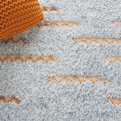 a blue rug with brown lines on it and an orange pillow next to it,