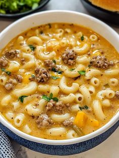 a bowl of pasta soup with meat and cheese in it next to a plate of bread