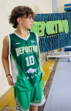 a young man standing in front of a sign wearing a green basketball jersey and shorts