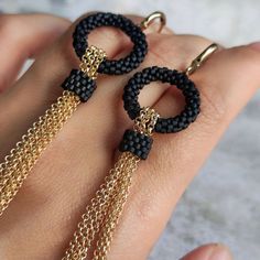 a pair of black and gold tasseled hoop earrings on someone's hand