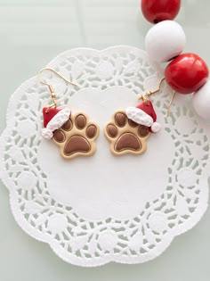 a pair of dog paw earrings with santa hat on them sitting on a doily