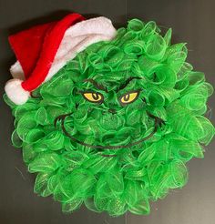 a green christmas wreath with a santa hat on it's head and yellow eyes