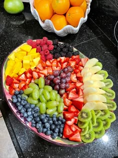 a platter filled with lots of fruit on top of a counter next to a bowl of oranges