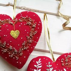 two red heart ornaments hanging from strings on a white wooden surface with gold trimmings