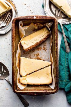 slices of cheesecake in a baking pan with spoons and forks on the side