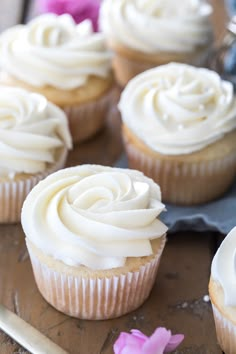 cupcakes with white frosting and pink flowers on a wooden table next to a knife