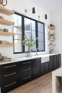 a kitchen with black cabinets and white counter tops is pictured in this image, there are shelves on the wall above the sink