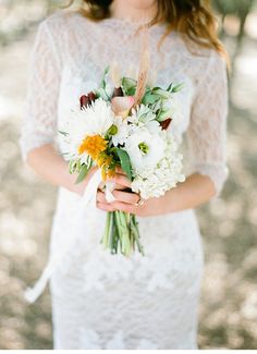 a woman holding a bouquet of white and orange flowers in her hands while wearing a lace dress