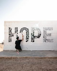 a man kneeling down next to a wall with graffiti on it's side and writing that says hope