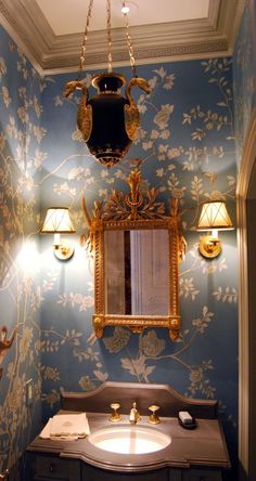 a fancy bathroom with blue walls and gold trimmings on the mirror above the sink