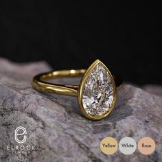 a yellow gold ring with a pear shaped diamond in the center on top of a rock