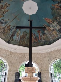 a cross in the middle of a church with stained glass windows on both sides and a painted ceiling above it