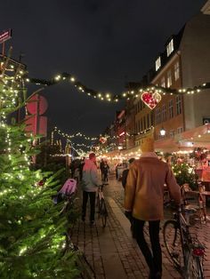 people are walking down the street with christmas lights strung over them and bikes parked on the sidewalk