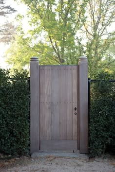 an open wooden gate in front of some bushes