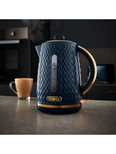 a black and gold coffee pot sitting on top of a counter next to a cup