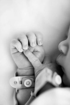 a black and white photo of a baby's hand holding the finger of his mother