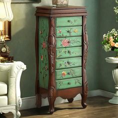 a green cabinet with flowers painted on it in a room next to a white chair