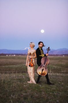 a man and woman standing next to each other in a field with an instrument on their back