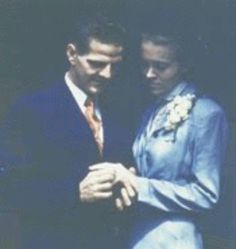 a man and woman standing next to each other in front of a black background with their arms around each other