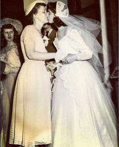 an old photo of two women kissing each other in front of some ladies wearing dresses and bonnets