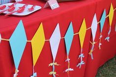 a red table topped with lots of paper kites on top of a grass covered field