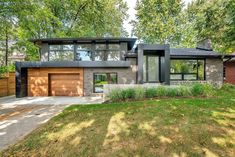 a modern house with large windows and lots of grass on the front lawn, surrounded by trees