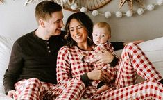 a man and woman are sitting on a bed with their baby in matching plaid pajamas