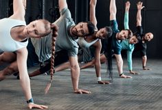 a group of people standing in a line doing yoga poses with their hands up and legs apart