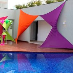 an outdoor swimming pool with colorful umbrellas and chairs on it's side, next to a white building