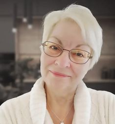 an older woman wearing glasses and a white sweater is smiling at the camera while standing in front of a kitchen