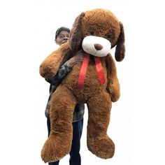 a man holding a giant stuffed dog in his arms and wearing a red ribbon around it's neck