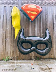 some balloons that are shaped like batman and superman mask on the side of a fence