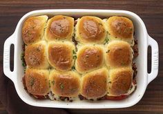 a white casserole dish filled with meat and cheese on top of a wooden table