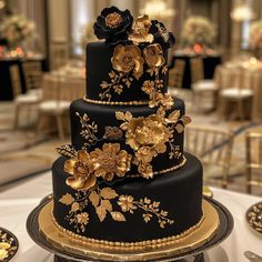 a three tiered black and gold wedding cake with flowers on the top is sitting on a table