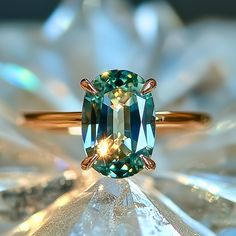 a fancy ring with an oval cut green and blue diamond in the center, on top of a white flower