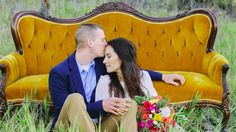 a man and woman sitting on an old couch in the grass with their arms around each other