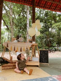 a baby sitting on the ground in front of a table with balloons and tassels