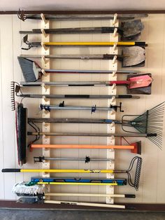 there are many different types of sports equipment hanging on the wall in this room, including brooms and rakes