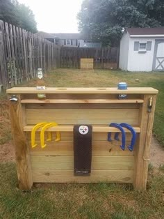 a wooden tool box with tools hanging from it's sides in the grass next to a fence