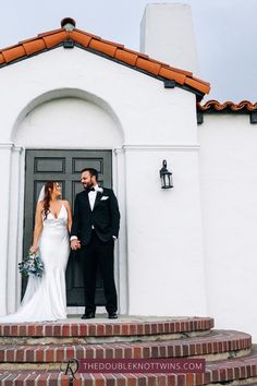 a bride and groom standing on steps in front of a white building with red tiled roof