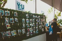 a woman standing next to a green wall covered in pictures and photos hanging on clothes pins