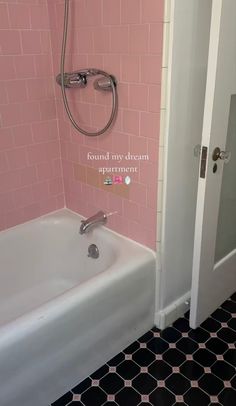 a bath tub sitting next to a door in a pink and black tiled bathroom with an open shower head