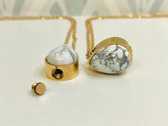 two pieces of jewelry sitting on top of a white table next to a gold chain