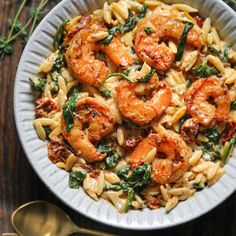 pasta with shrimp and spinach in a white bowl on top of a wooden table