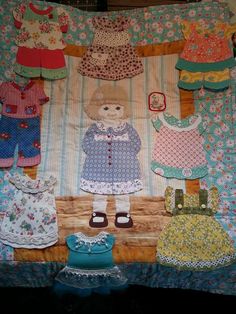 a teddy bear is standing in front of some baby clothes on a quilted blanket