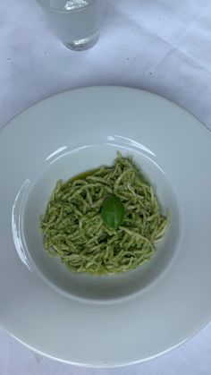 a white plate topped with pasta and pesto on top of a table next to a glass of water