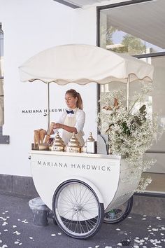 a woman standing behind a white cart with food on it's back and flowers in the front