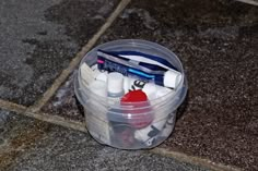 a plastic container filled with different types of toothbrushes and other items sitting on the ground